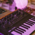 A Korg synthesizer illuminated with purple ambient lighting on a table setup.